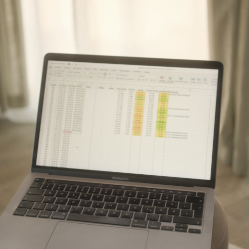 Open MacBook displaying a spreadsheet with color-coded data in a softly lit room.